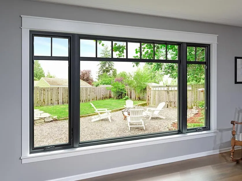 Wide black frame picture and casement window overlooking a landscaped backyard